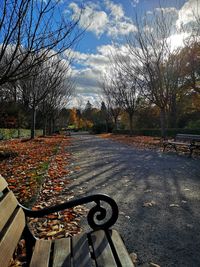 Park bench by road against sky during autumn