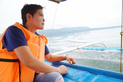 Side view of mature woman looking away while sitting in boat on sea against sky