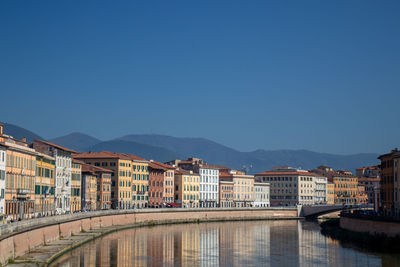 Buildings by river against clear blue sky