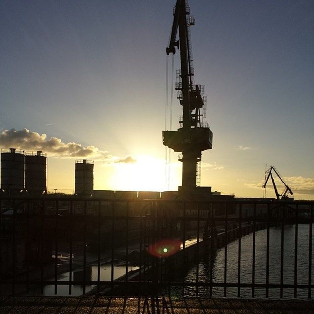 sunset, sun, crane - construction machinery, sunlight, silhouette, sky, built structure, architecture, construction site, sunbeam, building exterior, low angle view, crane, lens flare, development, orange color, industry, outdoors, metal, clear sky