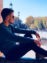 Young man looking away while sitting on retaining wall