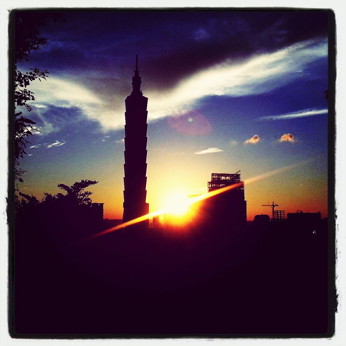 architecture, building exterior, sunset, built structure, sky, transfer print, silhouette, low angle view, cloud - sky, auto post production filter, tower, sun, orange color, cloud, city, sunlight, building, tall - high, outdoors, no people