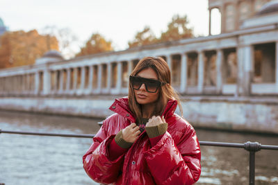 Woman wearing sunglasses standing by railing against bridge