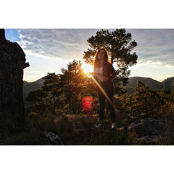 Woman standing by tree against sky during sunset