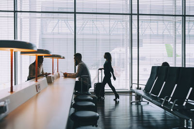 Businesswoman walking with luggage by window at airport departure area