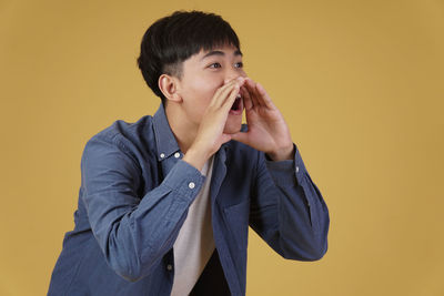 Portrait of young man standing against yellow background