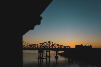 Silhouette bridge over river against clear sky during sunset