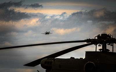 Silhouette helicopter against airplane flying in cloudy sky during sunset