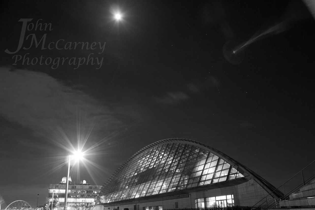 illuminated, night, low angle view, sky, built structure, lighting equipment, street light, architecture, text, transportation, communication, light - natural phenomenon, building exterior, outdoors, western script, city, cloud - sky, moon, dusk, silhouette