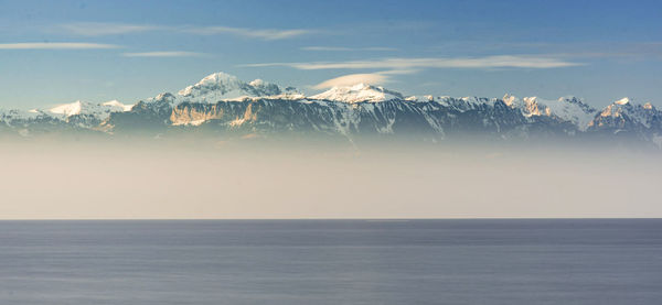 Scenic view of sea and snowcapped mountains against sky