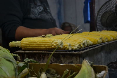 Midsection of vendor by sweetcorns for sale at market stall