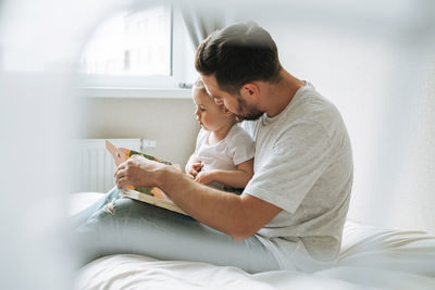 Happy father and baby girl little daughter having fun reading a book in children room at home