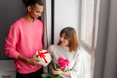 A stylish guy gives his girlfriend, a white heart-shaped box with a bow and a bouquet of roses