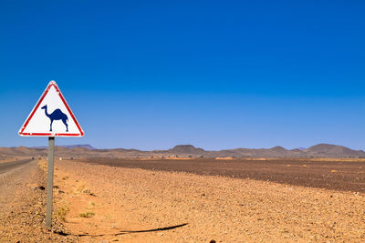 Road sign in desert against clear blue sky