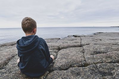 Rear view of man sitting on shore at beach against sky