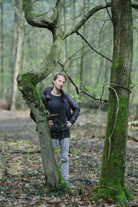 A young blond women in a forest at a tree with fresh and dark green.