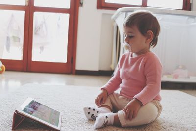 Cute girl looking at digital tablet on rug at home