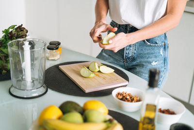 Young slim woman in white t-shirt and jeans cooking smoothie with apples healthy food in kitchen 