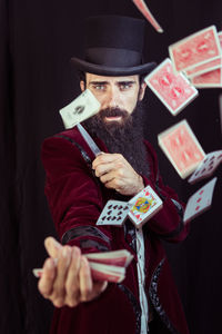 Portrait of magician throwing cards against black background