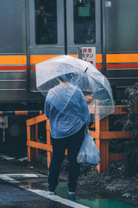 Rear view of man walking on wet street during rainy season