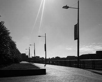 Silhouette street lights on footpath in city against sky