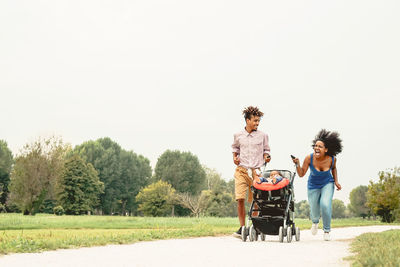 Cheerful family laughing while walking in park against sky