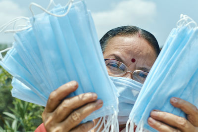 Portrait of an aged indian woman showing bundles of blue coloured surgical face masks in hand.