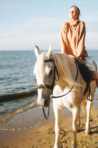 Young woman in beige sweater with white horse on seascape background