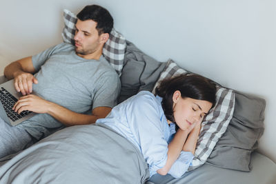 High angle view of woman sleeping while man using laptop on bed at home