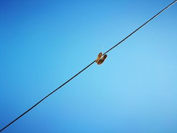 Low angle view of shoes hanging on cable against clear blue sky