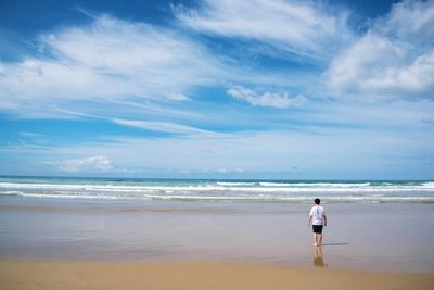 Rear view of man standing on beach against sky