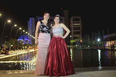 Portrait of friends standing on retaining wall against pond at night