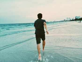 Rear view of man on beach against sky