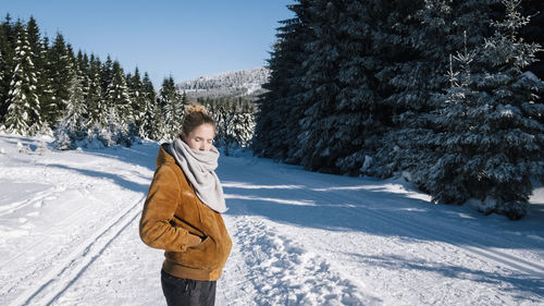 Side view of young woman wearing warm clothing while standing on snow covered land