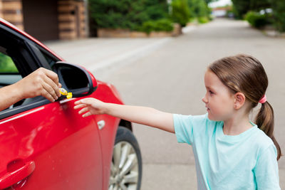 Cropped hand of man giving candy through car window to daughter standing on road