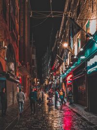 People walking on wet road in city during rainy season at night