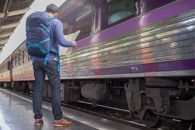 Full length of man holding map while standing at railroad station platform