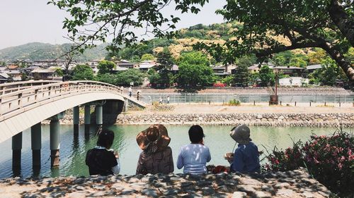 Rear view of people sitting on riverbank against sky