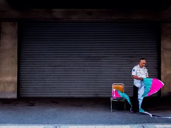 Security guard holding plastic while standing against closed shop shutter