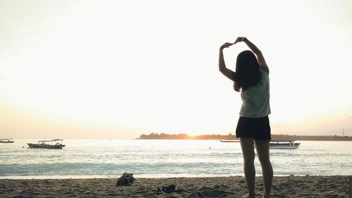 Rear view of woman standing at beach against clear sky