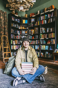Portrait of smiling young man sitting on floor with books in bookstore