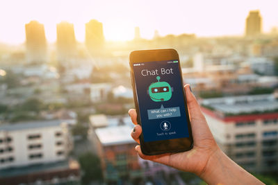 Close-up of hand holding smart phone against cityscape