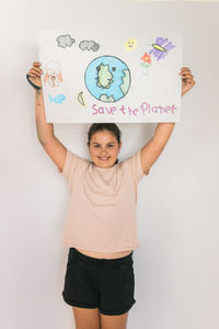 Smiling girl with arms raised holding poster at home