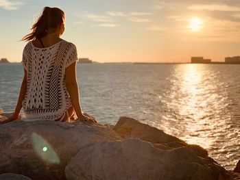 Woman sitting on rock by sea against sky