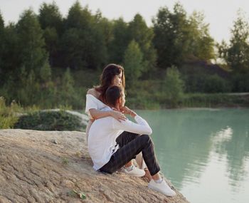 Rear view of woman sitting on lake against trees