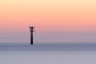 Silhouette tower by sea against sky during sunset