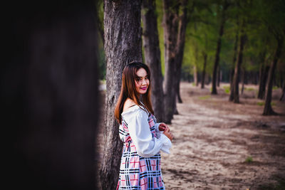 Portrait of woman standing by tree trunk in forest