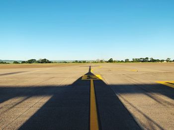 Shadow of airplane on runway against clear blue sky