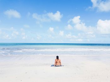 Rear view of woman sitting at beach against sky