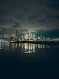 Illuminated buildings by river against sky at night